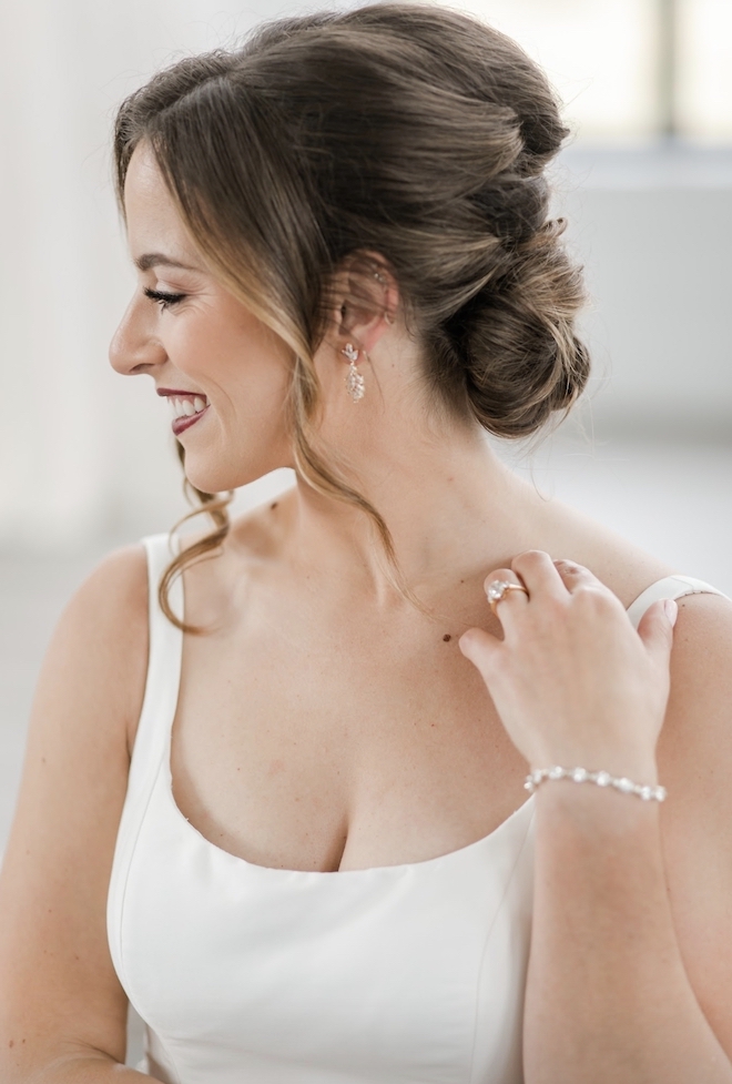 Bride dressed in a white wedding gown, glam makeup look, and an up-do hairstyle with curls. 