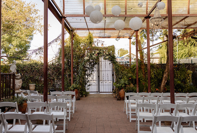 Outdoor venue with lush greenery, white hanging lights, and white chairs. 