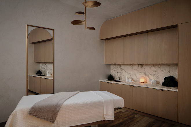 A massage room with a white massage bed with wooden cabinets and a marble backsplash. 