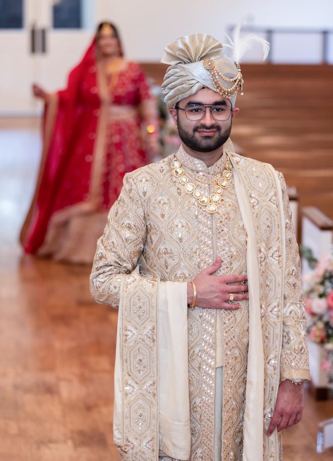 The groom wearing gold and the bride standing behind him in red right before the first look. 