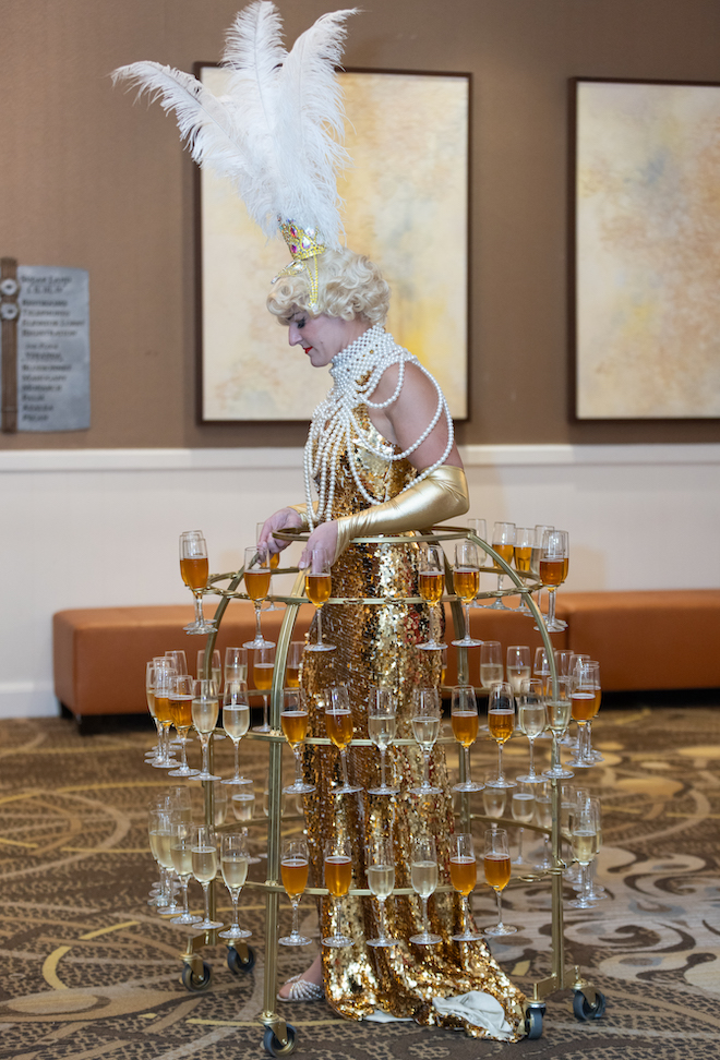 A person wearing a gold dress with a champagne holder. 